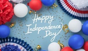 The image says Happy Independence Day in white script on a blue background, surrounded by red, white, and blue balloons, ribbons, paper fans, and confetti.